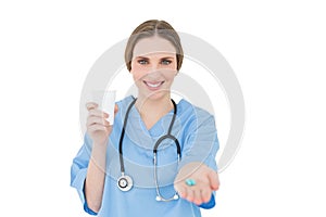 Pretty female doctor holding a plastic cup and handing blue pills