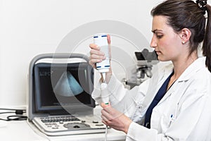 Pretty female doctor, posing while is doing a sonography. Female doctor wearing white coat, holding a ultrasound device