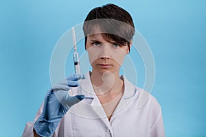 Pretty female doctor wearing white medical robe holding syringe at blue background. treatment and prevention coronavirus