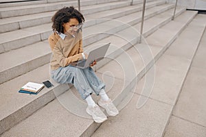 Pretty female entrepreneur working on laptop sitting outside on modern building background