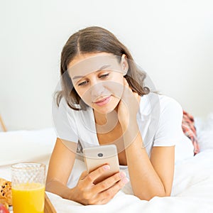 Pretty female looking social media on mobile phone laying in bed. Natural realistic beauty