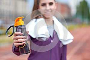 Pretty female runner resting and drinking water from a bottle after working out track run of stadium