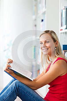 Pretty female student with books working in a high school library