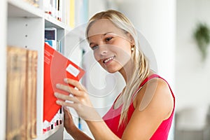 Pretty female student with books working in a high school library