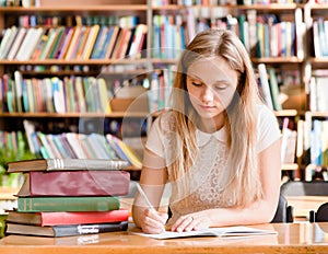 Pretty female student with books working in a high school library