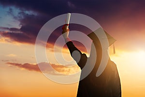 A pretty female student, celebrating her graduation and stand against the idyllic sunset view with holding her diploma