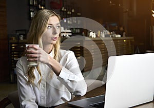 Pretty female student with cute smile keyboarding something on net-book and enjoying cappuccino. Beautiful happy woman