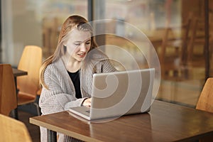 Pretty female student with cute smile keyboarding something on net-book while relaxing after lectures in University