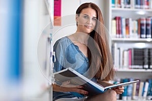 Pretty female student with laptop and books working in a high school library