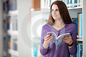 Pretty female student with laptop and books working in a high school library