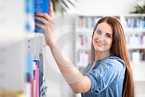 Pretty female student with laptop and books working in a high school library