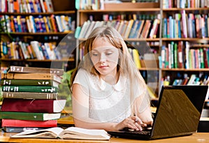 Pretty female student typing on notebook in library