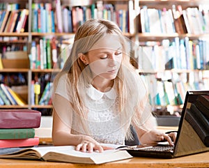 Pretty female student typing on notebook in library