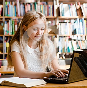 Pretty female student typing on notebook in library