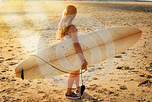 pretty female surfer with her long board under her arm looking at the waves in the evening