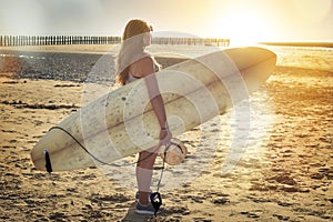 pretty female surfer with her long board under her arm looking at the waves in the evening