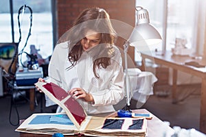 Pretty female tailor choosing a fabric in cloths catalog in studio