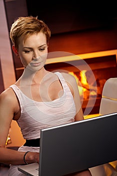 Pretty female using laptop by fireplace