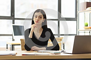 Pretty female worker looks forward at workplace in office