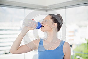Pretty fit woman drinking water on her plastic flask