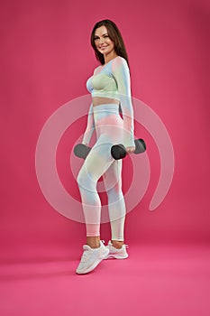 Pretty fitness girl posing with heavy dumbbells indoors.