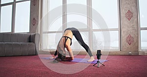Pretty, flexible girl practicing yoga pose barefoot on yoga mat at home, in apartment.