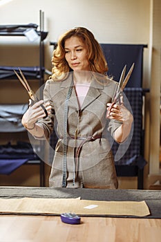 Pretty focused young woman fashion designer cutting grey fabric in studio