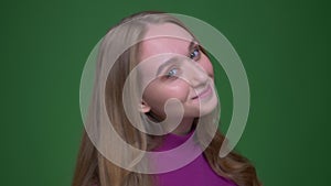 Pretty ginger female student shakes her hair and watches prettily into camera on green chroma background.