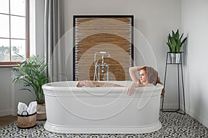 Pretty ginger woman lying in a bath and looking relaxed