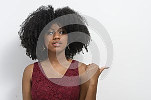 The pretty girl with afro hair points her thumb to the right side in the copy space, announces the product, red colored dress .  Y