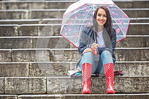 Pretty girl awaits her date sitting on stone stairs protecting herself from rain by an umbrella