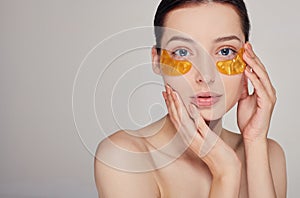 Pretty girl on the background applying golden collagen patches under the eyes