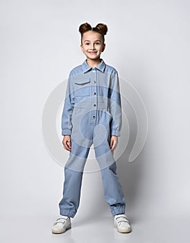 pretty girl with bagel hairdo standing straight in blue cotton summer jumpsuit with comfortable pockets. on a light