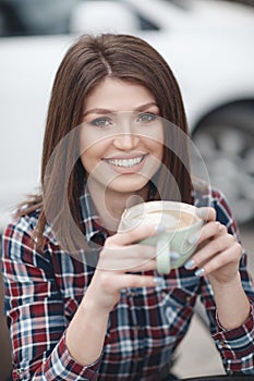Pretty girl, beautiful brunette with elegant hairstyle in a plaid shirt drinks cup of coffee outdoors in summer cafe
