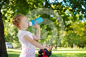 Pretty girl with bicycle drinks water in summer park