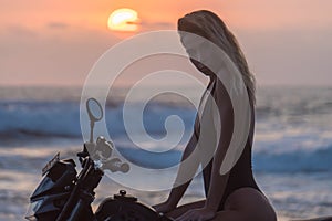 Pretty girl in black bikini posing on racing autobike, girl against evening sky photo