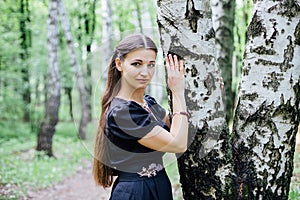 Pretty girl in black Russian dress with embroidery leaned against birch