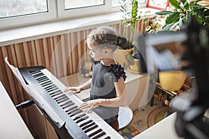 Pretty girl blogger playing classic digital piano and recording video like online concert at home
