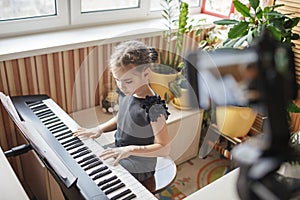 Pretty girl blogger playing classic digital piano and recording video like online concert at home