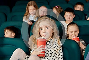 Pretty girl with blonde hair drinking cola in cinema.