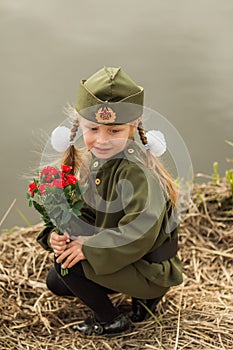 Pretty girl with a bouquet of flowers sitting by the river in uniform on the day of victory in sorrow