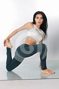 A pretty girl brunette stretching instructor, yoga, trainer, danser, posing in the studio on a white background in lasins and T-