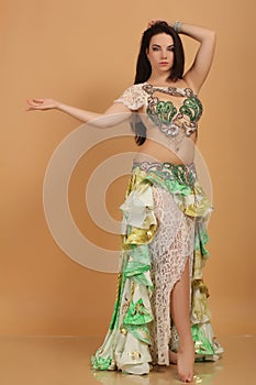 A pretty girl brunette who dances go-go and belly dance, stretching posing in studio in green arabian dress on a beige background