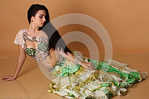 A pretty girl brunette who dances go-go and belly dance, stretching posing in studio in green arabian dress on a beige background