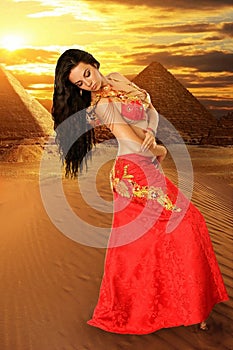 A pretty girl brunette who dances go-go and belly dance, stretching posing in studio in red arabian dress on a white background