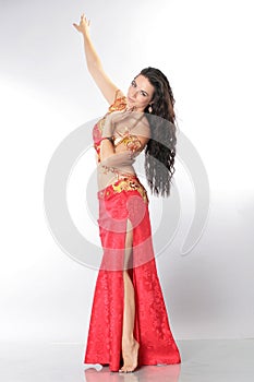 A pretty girl brunette who dances go-go and belly dance, stretching posing in studio in red arabian dress on a white background