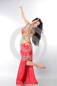A pretty girl brunette who dances go-go and belly dance, stretching posing in studio in red arabian dress on a white background
