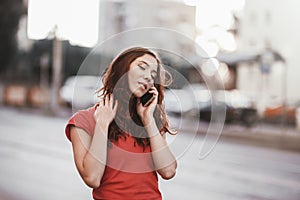 Pretty girl in casual dress is talking on a mobile phone while walking at the city street on a sunset time.