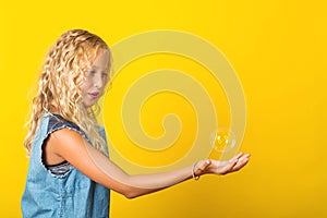 Pretty girl catch soap bubble over yellow background. Blonde girl with curly healthy hair. Summer fashion