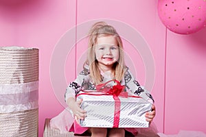 Pretty girl child 3 years old in a dress. Baby holding gift in their hands. Rose quartz room decorated holiday